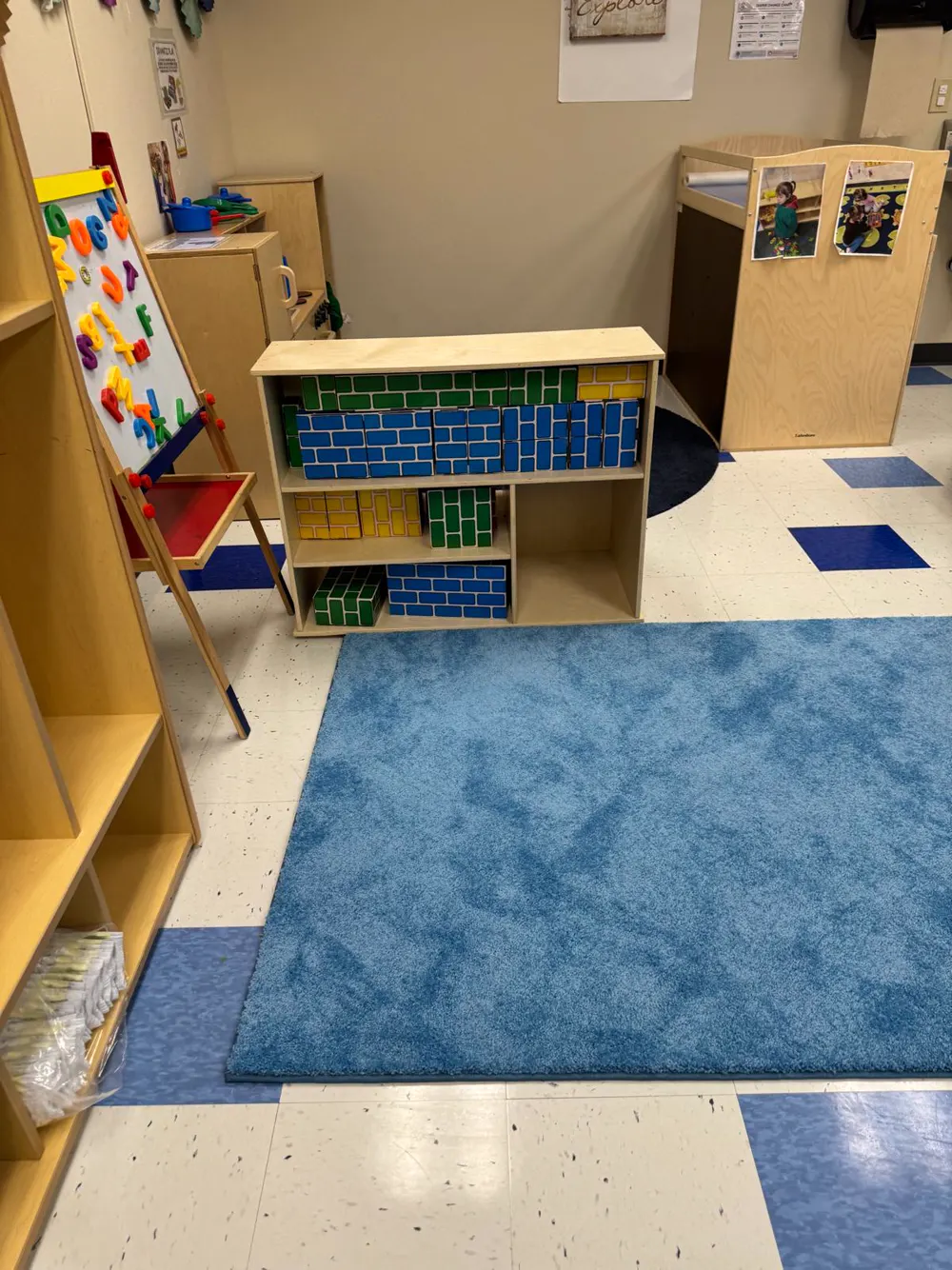 Toddler room with a blue rug, art easel and building block shelf