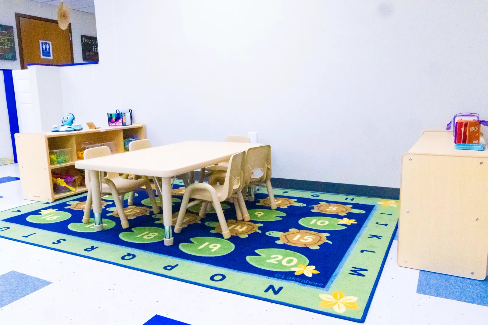 Clean, bright classroom with an alphabet rug, a table and chairs, and toy shelves