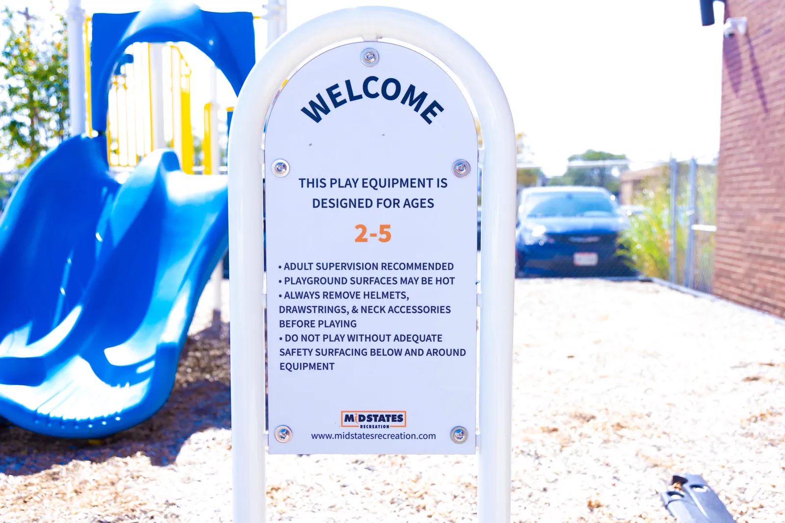 Outdoor playground with a blue slide and a welcome sign for ages 2 to 5